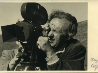 Historische Schwarzweiss-Fotografie: Mann mit Brille blickt durch eine professionelle Filmkamera im Freien