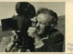 Historische Schwarzweiss-Fotografie: Mann mit Brille blickt durch eine professionelle Filmkamera im Freien