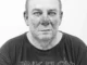 Schwarzweiss-Porträtfotografie: Mann mit staubbedecktem Gesicht und Pink-Floyd-Shirt vor weissem Hintergrund
