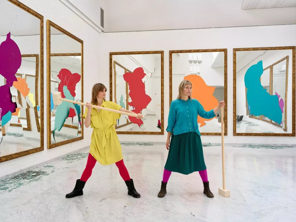 Elina Brotherus, Fill with Own Imagination: Zwei Frauen mit Holzstangen vor zerbrochenen Spiegeln mit bunten Farbformen