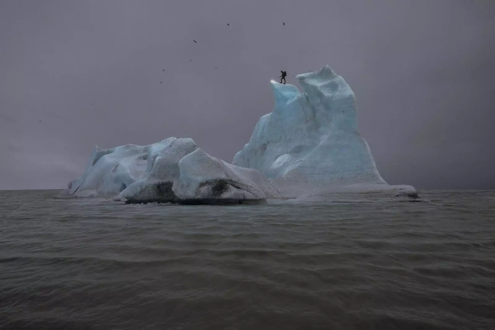 Julian Charrière Wolfsburg – Fotografisches Kunstwerk: Menschliche Silhouette auf eisblauem Eisberg im grauen Polarmeer, Vögel im Nebel