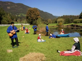 Ragnar Kjartansson, Sunday Without Love: Musiker in blauen Kitteln und Frauen in Tracht auf sommerlicher Almwiese mit Teich