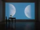 Videoinstallation: Zwei Mondphasen auf blauer Projektionswand, davor antiker Tisch mit Öllampe und Stuhl