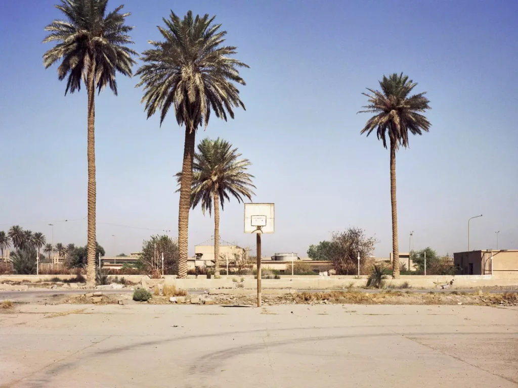 Verlassener Basketballplatz mit verwittertem Korb, Palmen und sandfarbenem Betonboden unter blauem Himmel